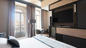Una habitación de hotel moderna con una cama grande, un televisor de pantalla plana montado en la pared, una pequeña mesa redonda y una lámpara de pie.