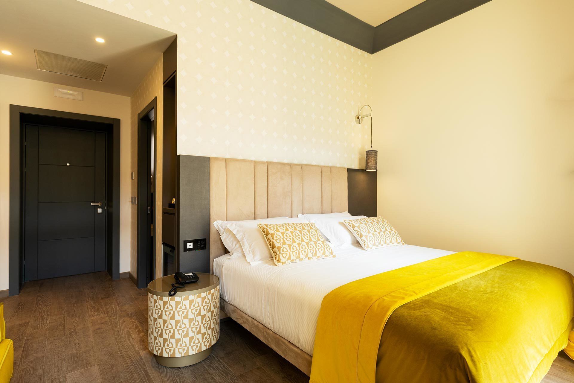 A hotel room with a bed, bedside table, and a door.