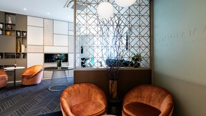 Un interior moderno con un diseño geométrico en la pared, una zona de estar con dos sillones acolchados, una mesa redonda y un jarrón decorativo con ramas.