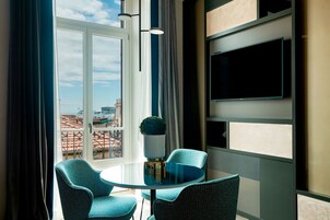 Una habitación moderna con una mesa de vidrio y dos sillas, un ventanal con cortinas y un televisor montado en la pared.