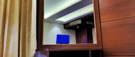 A room with a large mirror, wooden walls, a patterned ottoman, and a television on a stand.