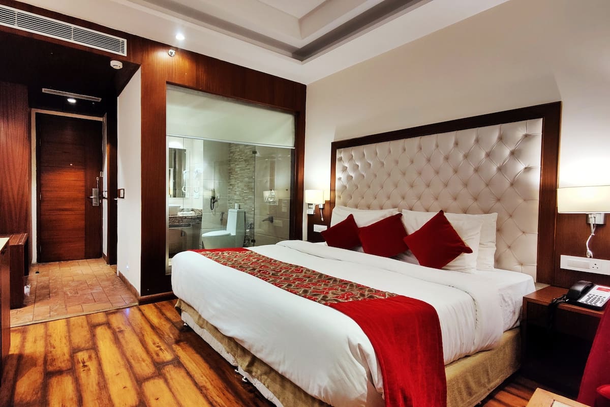 A hotel room with a large bed, a wooden desk, a glass-enclosed shower, and a red chair.