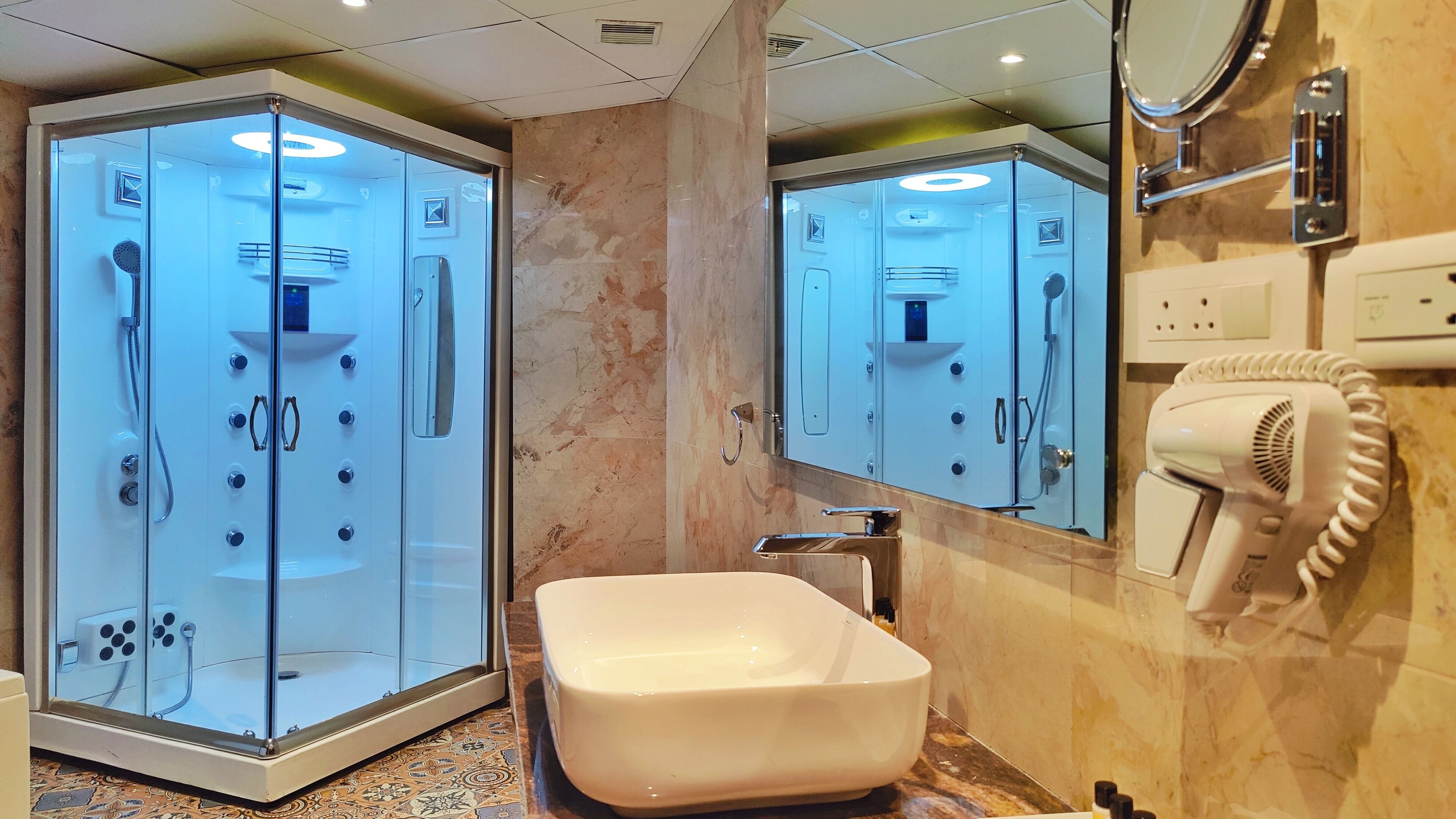 A modern bathroom with a glass-enclosed shower, a large sink, and a hairdryer mounted on the wall.
