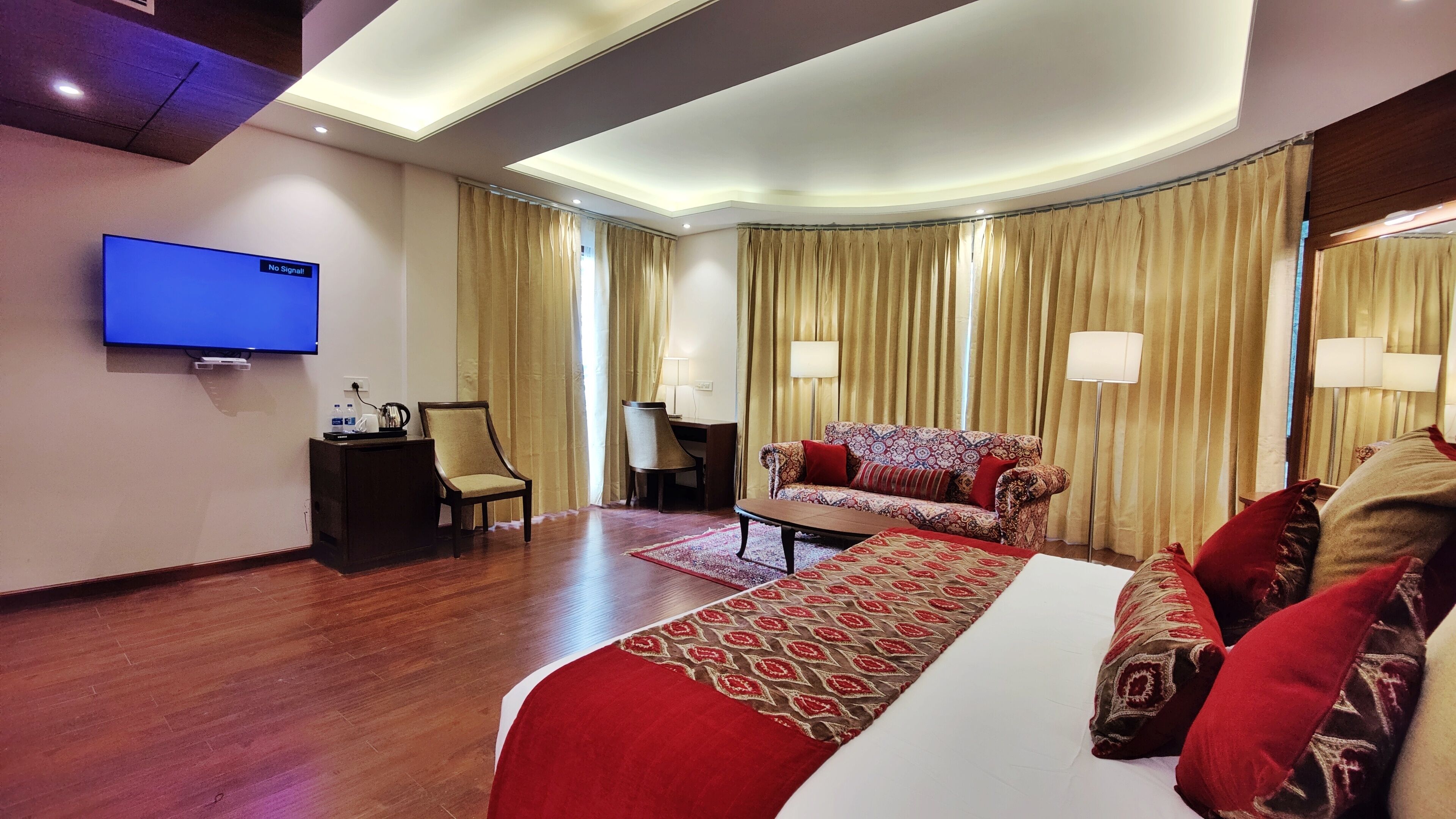 A hotel room with a large bed, a sofa, a desk, a TV, and curtains.