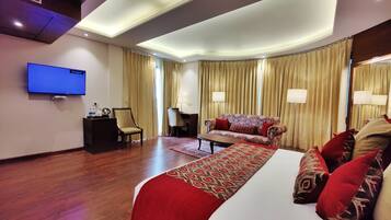 A hotel room with a large bed, a sofa, a desk, a TV, and curtains.