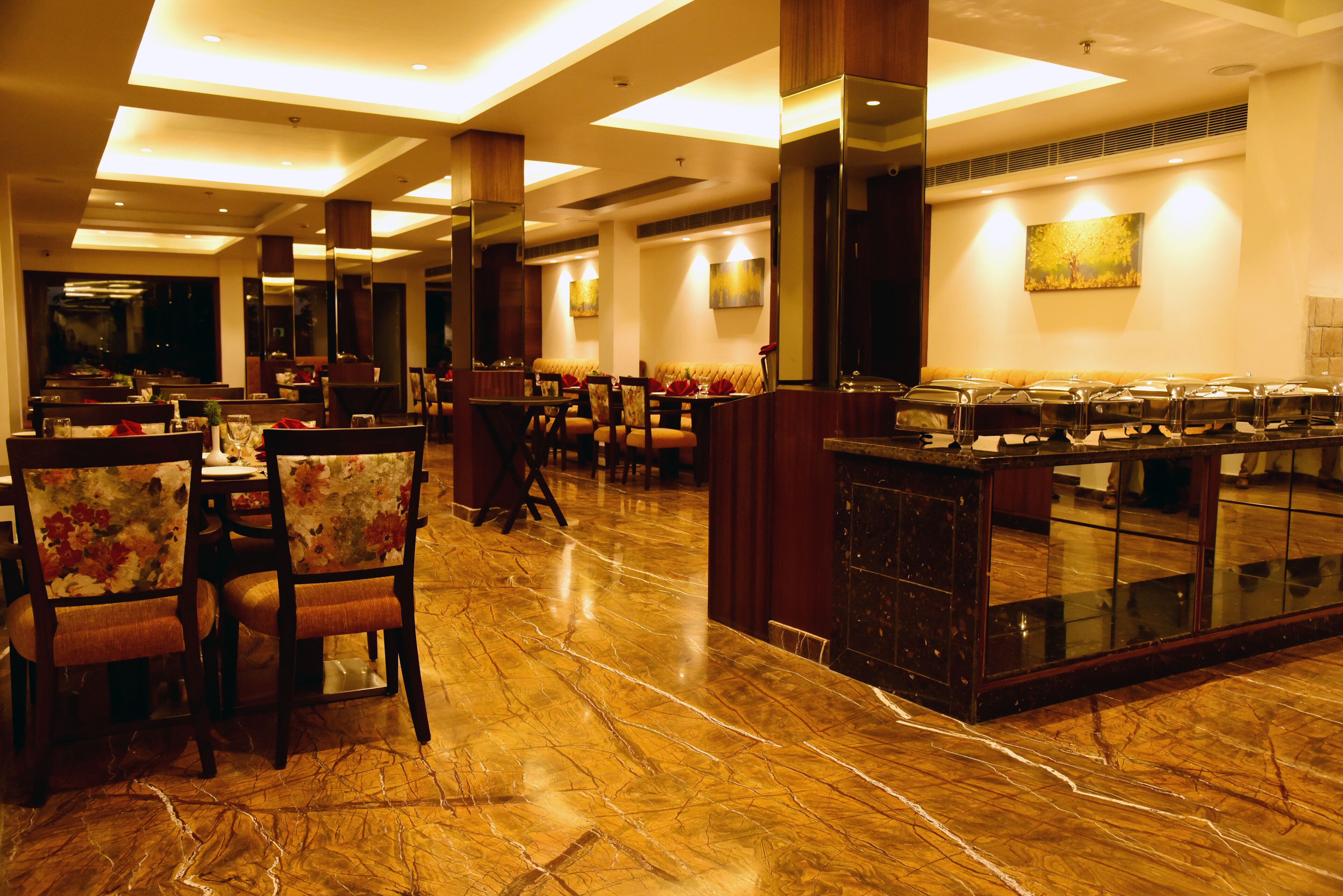 A spacious hotel dining area with marble flooring, wooden chairs, and a buffet counter.