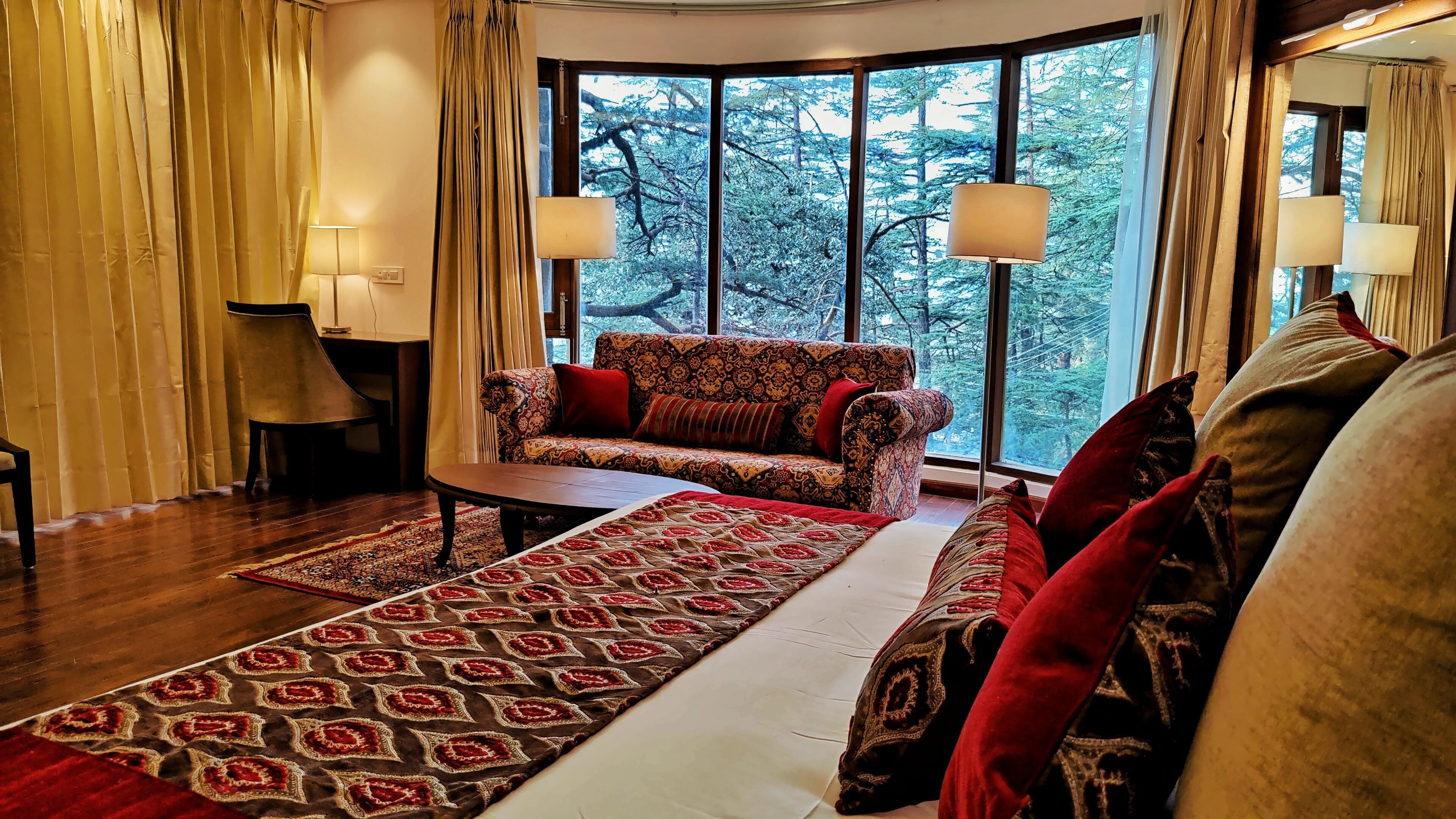 A cozy living room with a patterned sofa, a coffee table, and a large window offering a forest view.