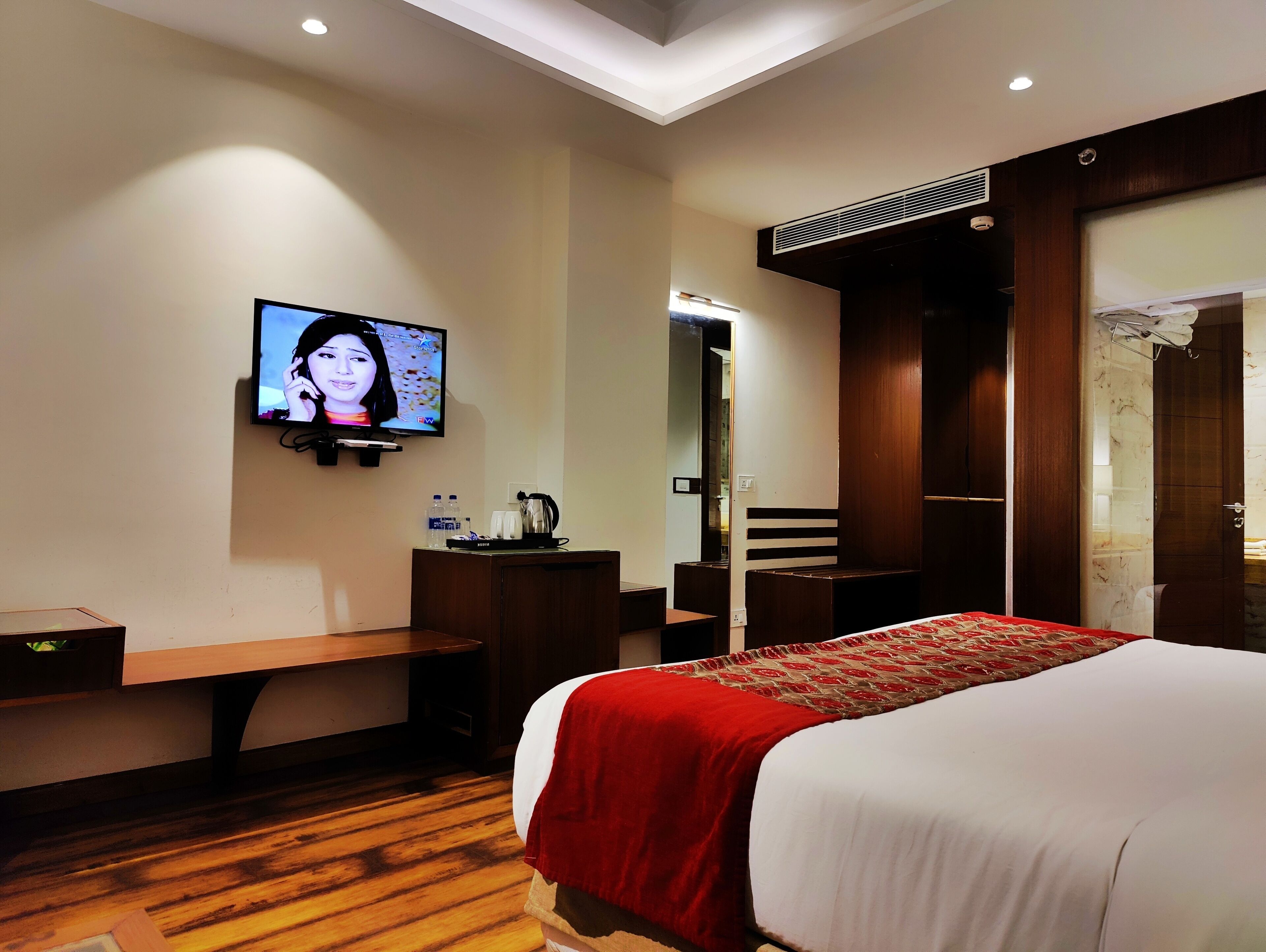 Habitación de hotel con cama, televisor montado en la pared, escritorio con silla y piso de madera.