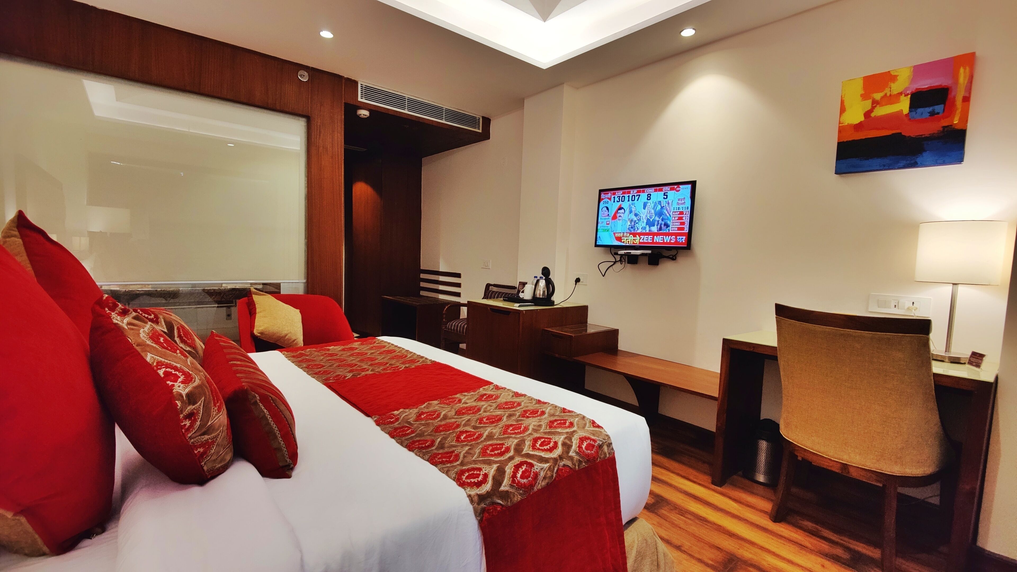 A hotel room with a bed, a desk, a chair, a TV, and a painting on the wall.