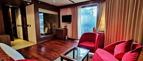Una sala de estar moderna con un sofá rojo, una mesa de centro de vidrio y una chimenea. Hay un televisor montado en la pared y una ventana con cortinas.