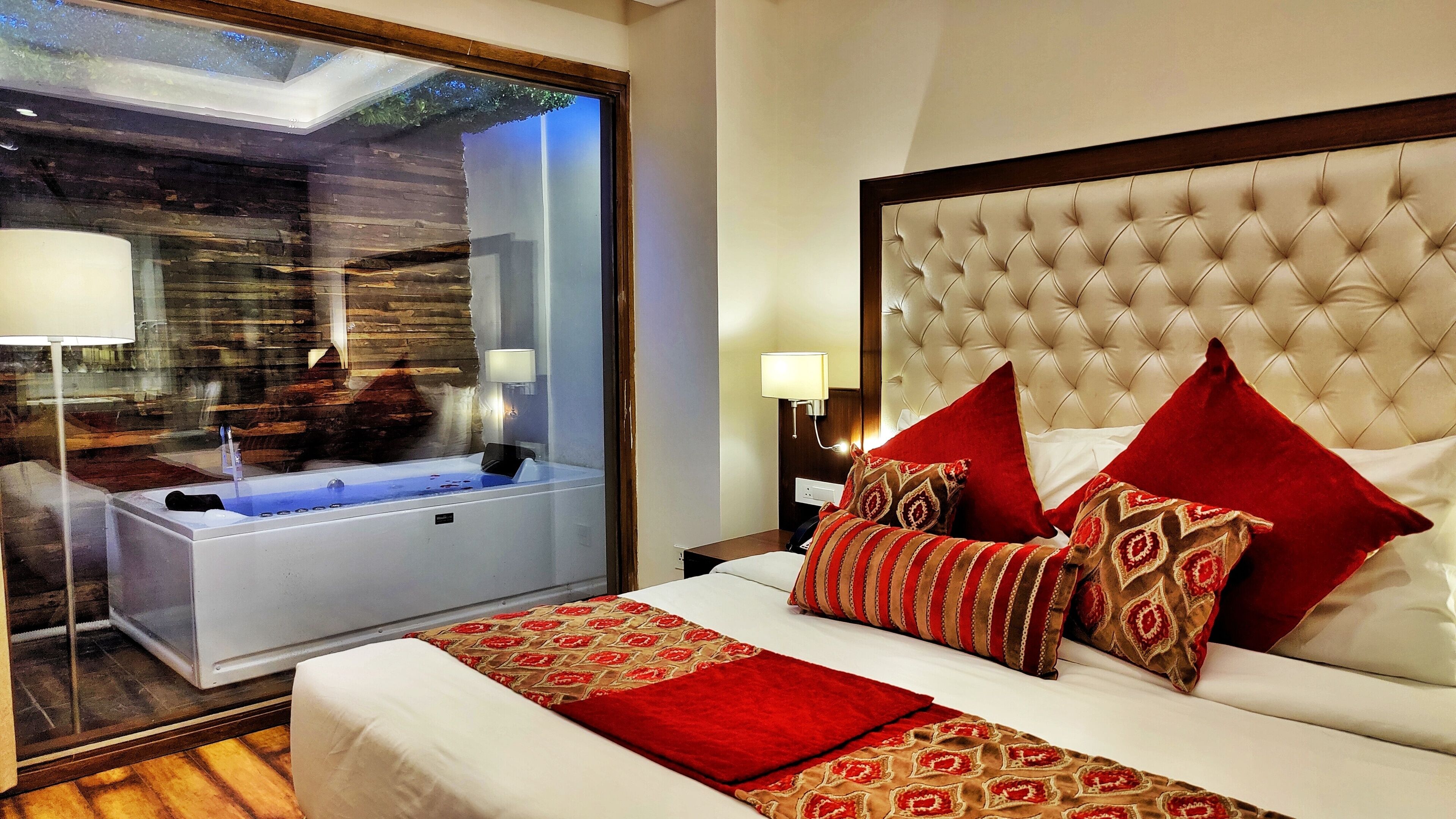 Quarto de hotel com uma cama grande, banheiro separado com banheira e vista para uma construção de madeira lá fora.