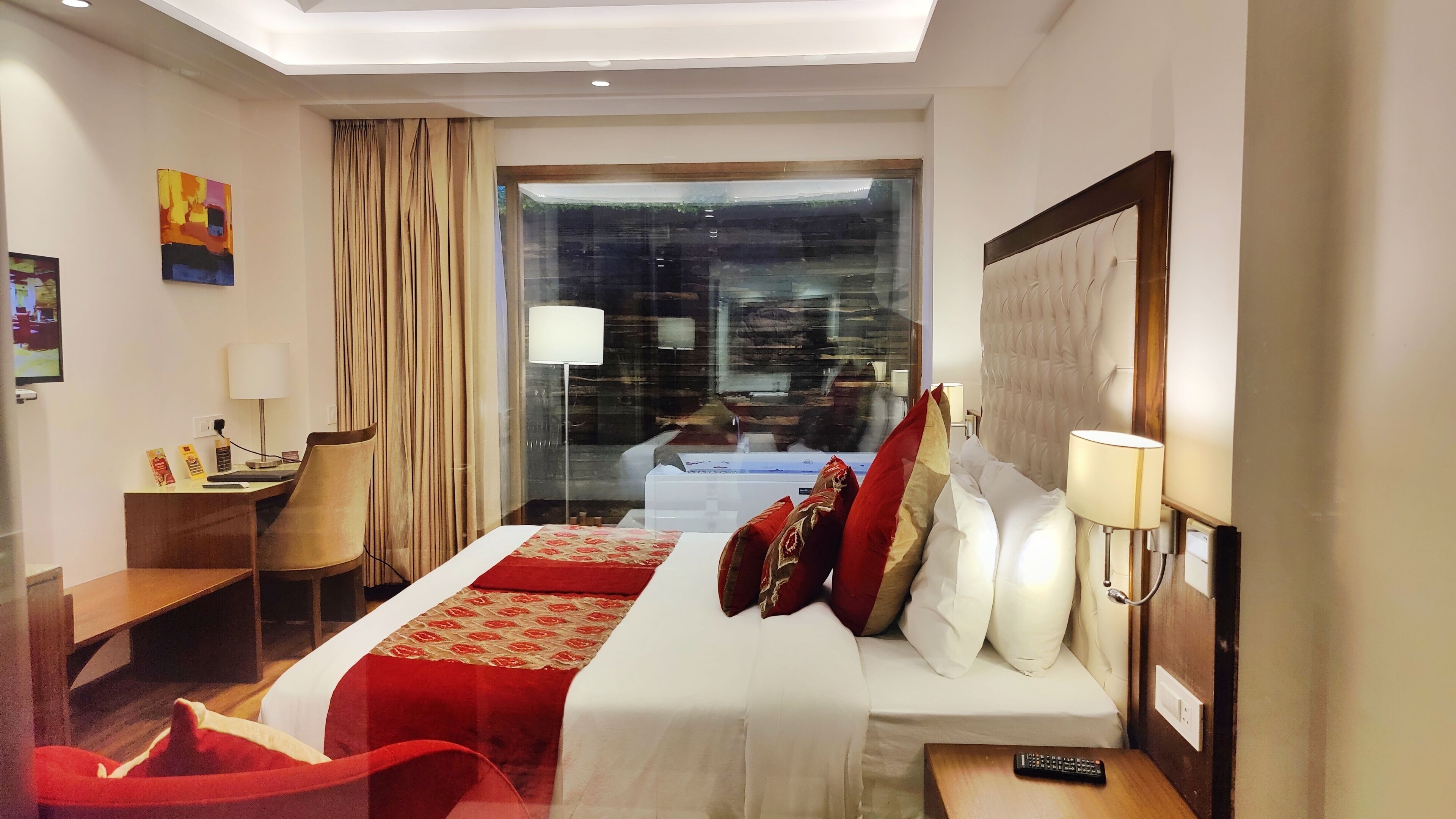 A hotel room with a large bed, a desk, a chair, a TV, and a window with curtains.