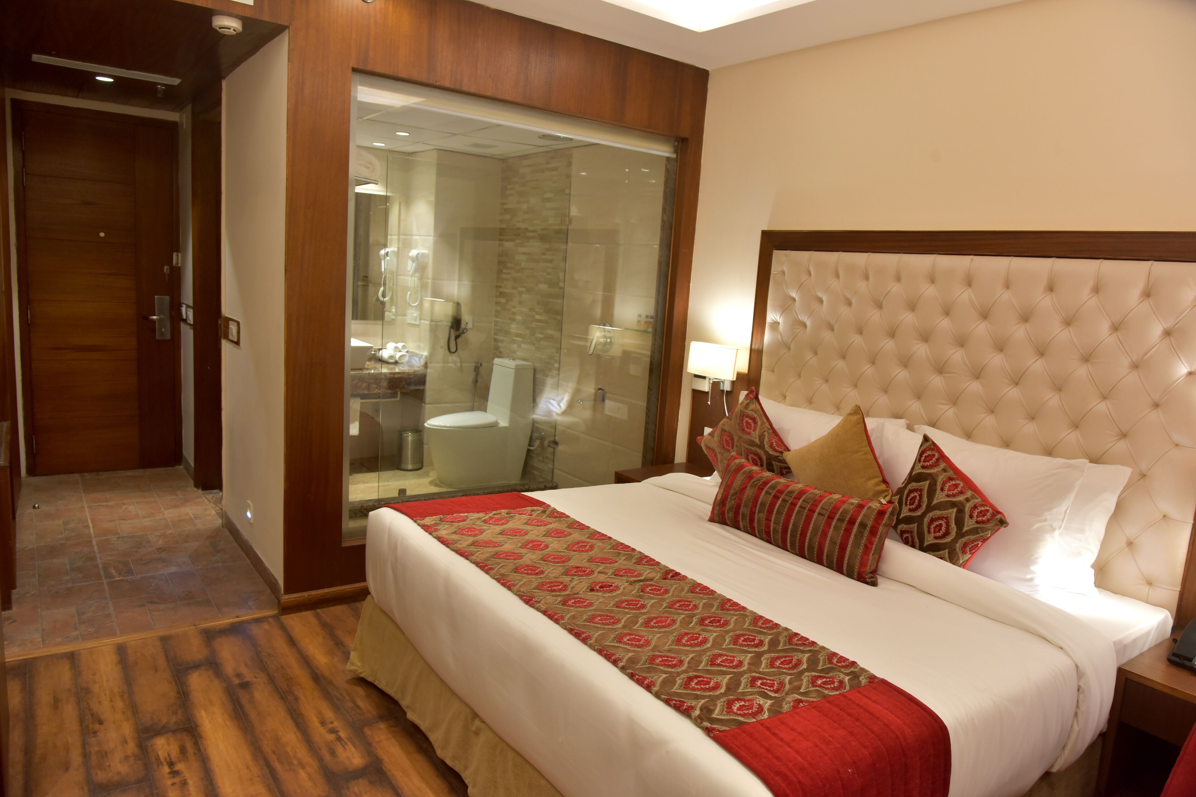 Habitación de hotel con una cama grande, cabina de ducha con paredes de vidrio y piso de madera.