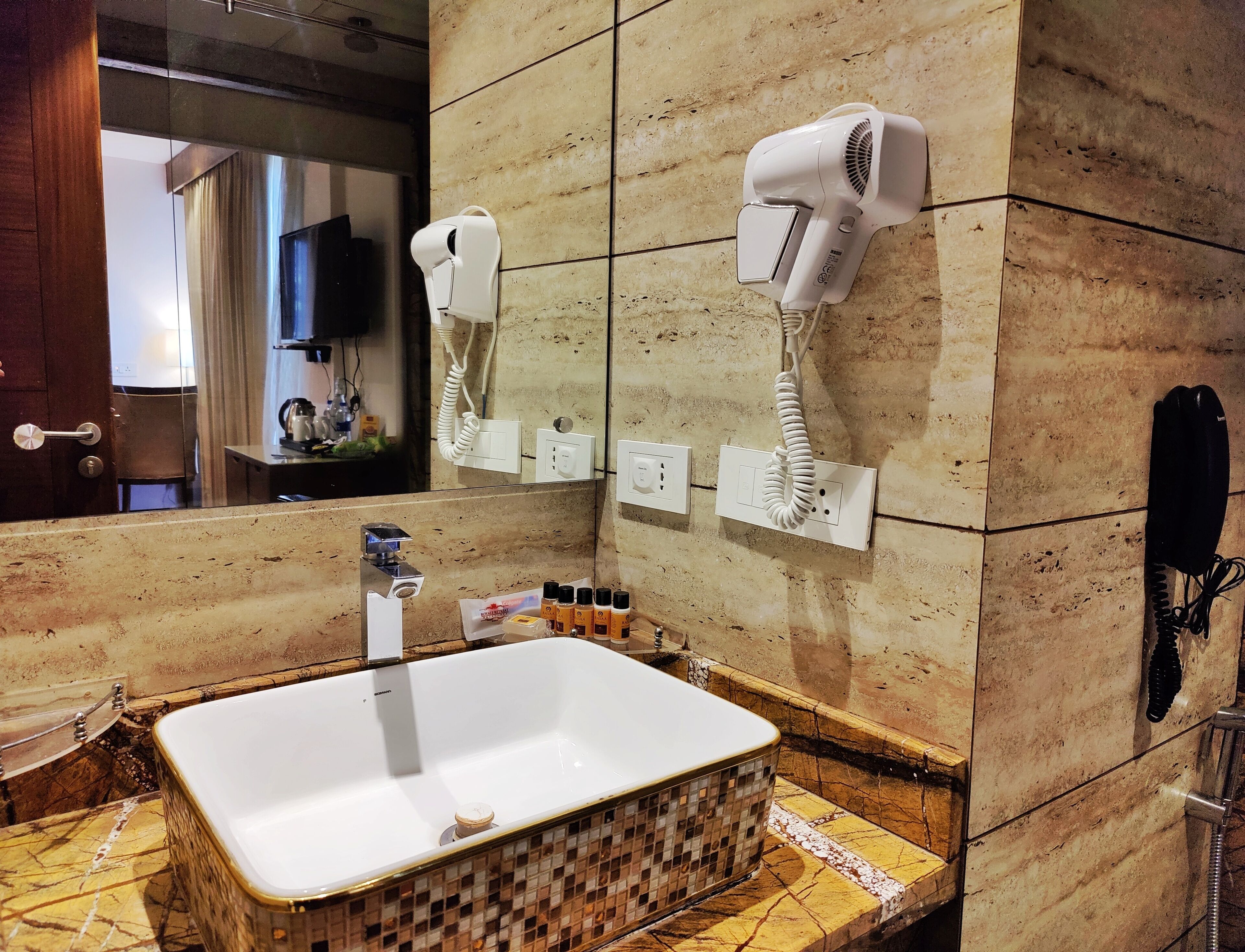 A bathroom with a large mirror, a sink, a hairdryer, and a telephone.