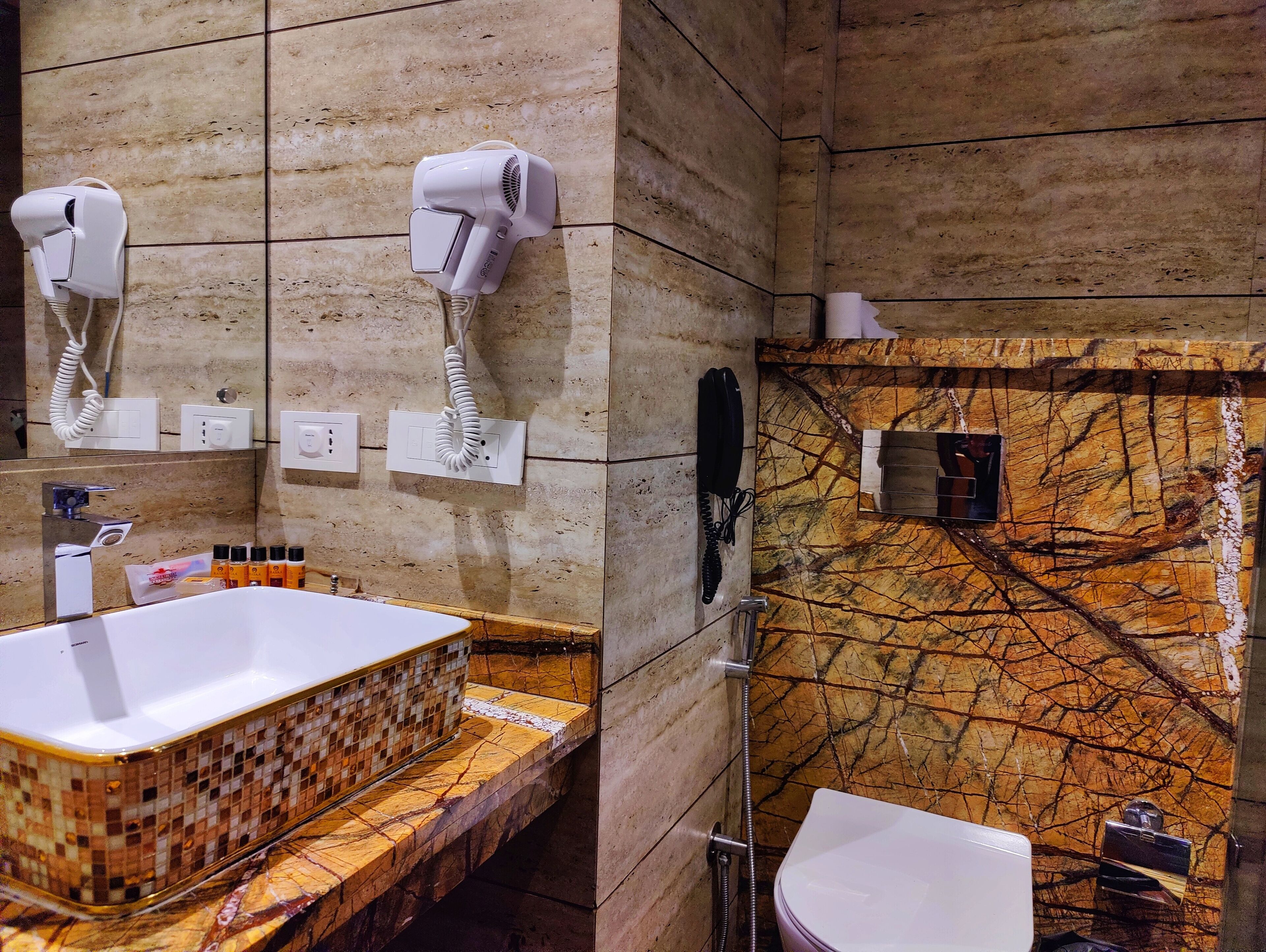 A bathroom with a marble sink, a hairdryer, a telephone, and a shower.