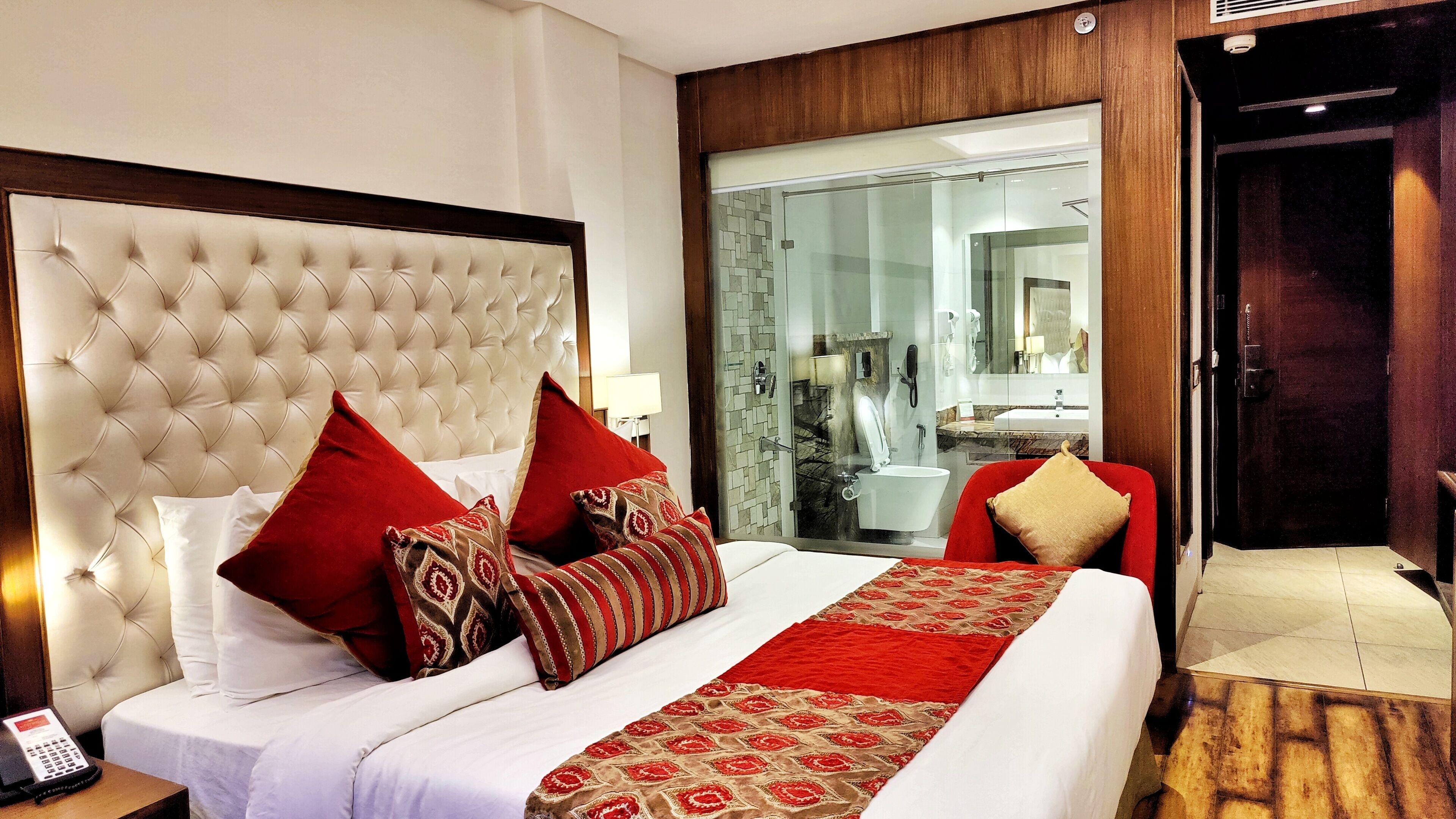 A hotel room with a large bed, a wooden headboard, and a view of the bathroom through a glass door.
