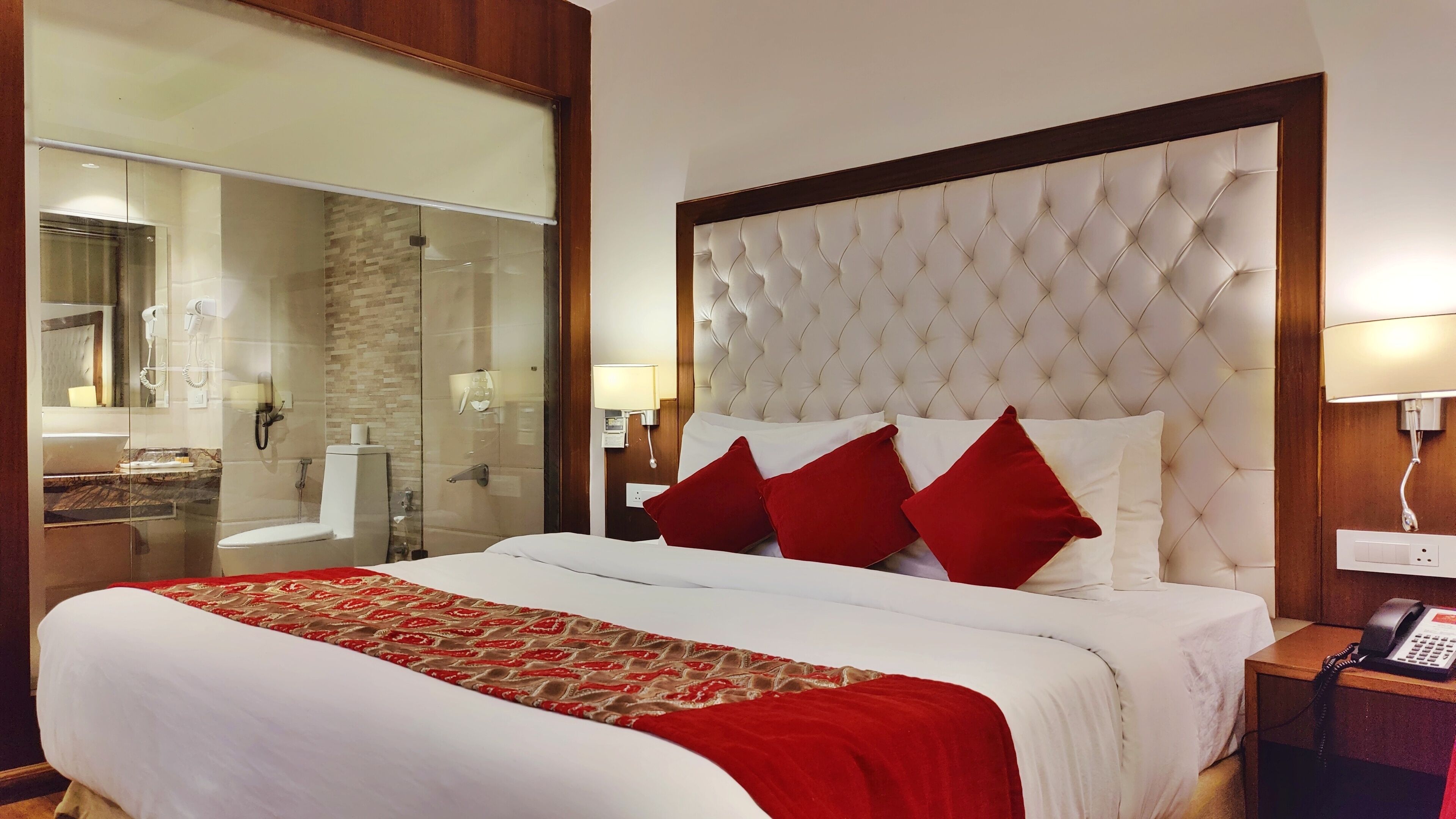 A hotel room with a large bed, a glass shower enclosure, a wooden headboard, and a bedside telephone.