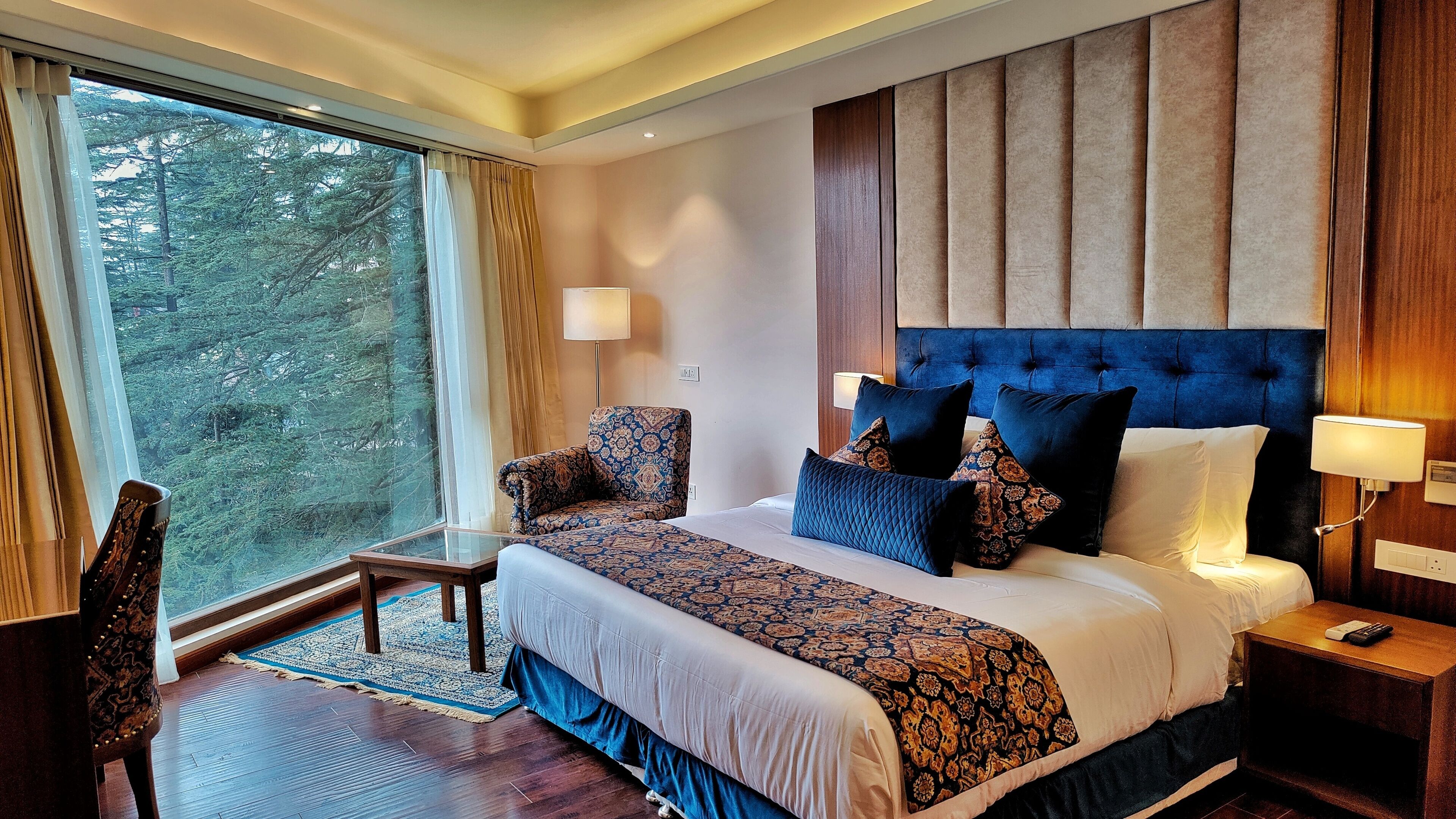 Hotelkamer met een groot bed, een stoel, een tafel en uitzicht op bomen.