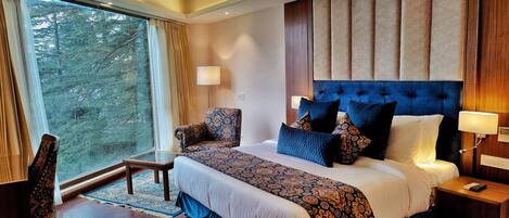 Une chambre d’hôtel avec un grand lit, une chaise, une table et une vue sur les arbres par la fenêtre.
