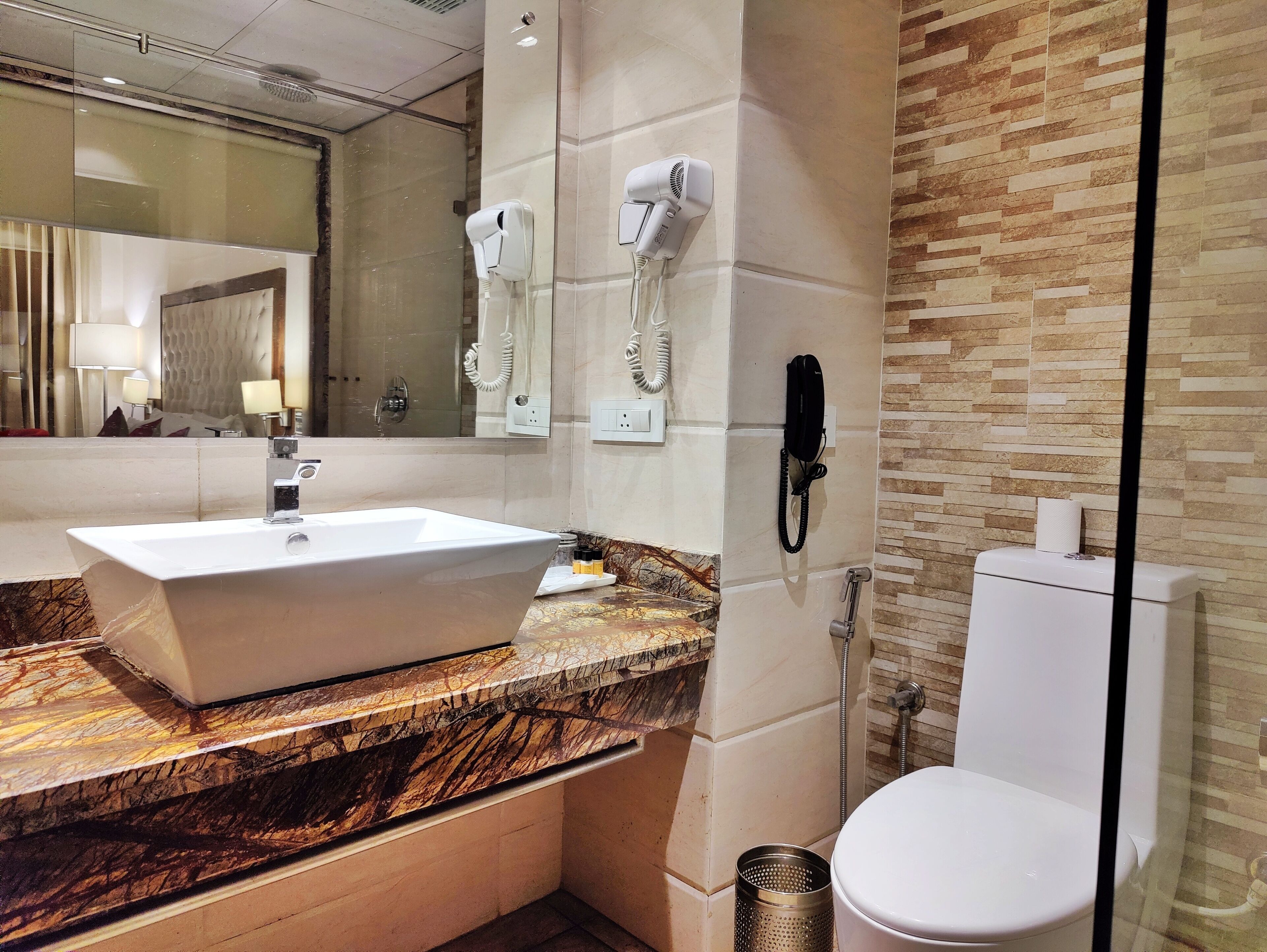 A modern bathroom with a marble countertop, a white sink, a glass shower enclosure, and a toilet.