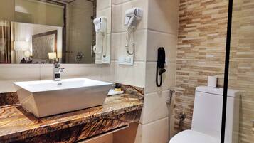 Une salle de bain moderne avec un comptoir en marbre, un lavabo blanc, une cabine de douche en verre et des toilettes.