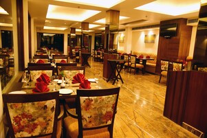 A restaurant with multiple dining tables and chairs, each set with red napkins and wine glasses.