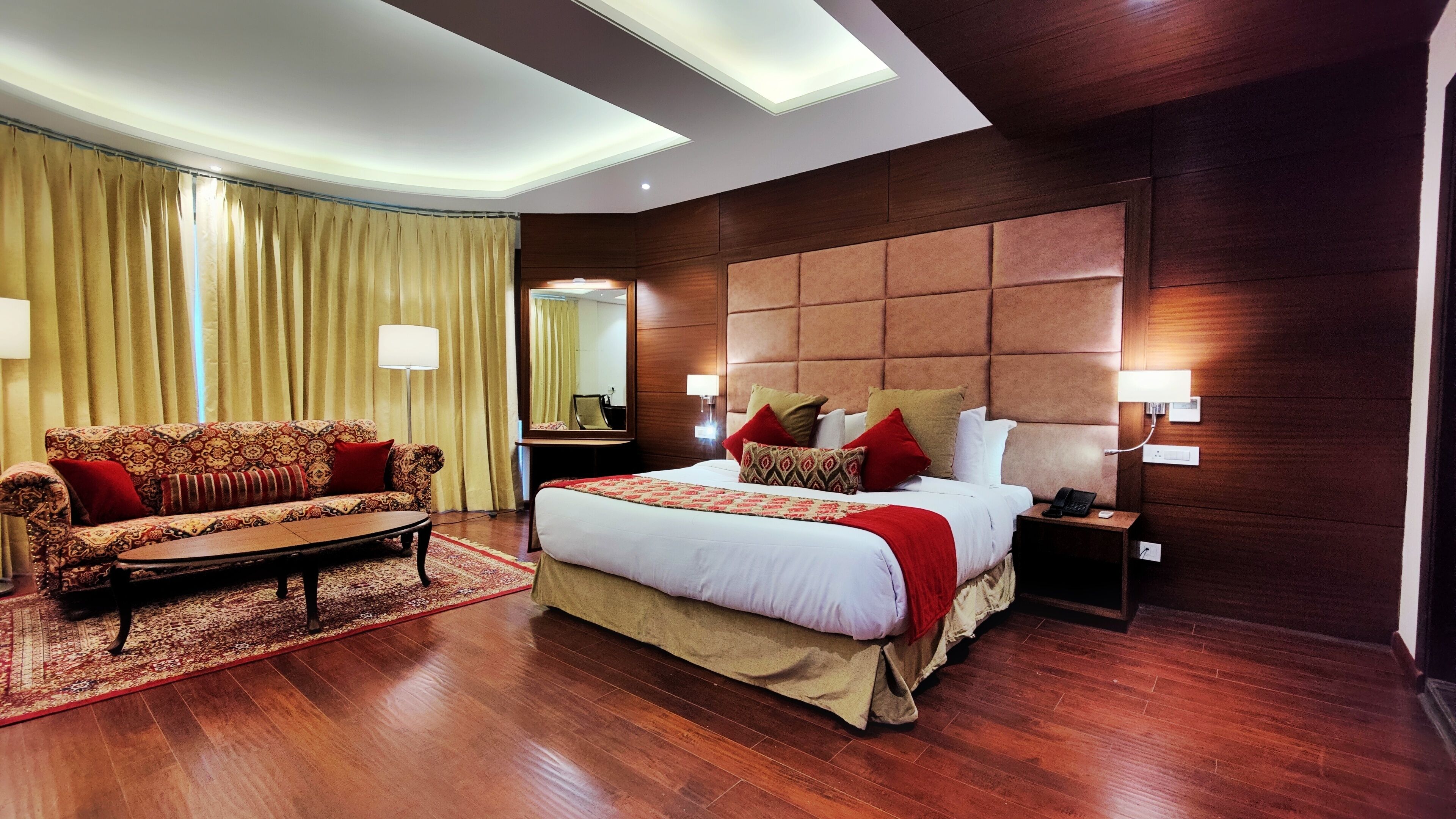 A hotel room with a large bed, a sofa, a nightstand with a phone, and a mirror.