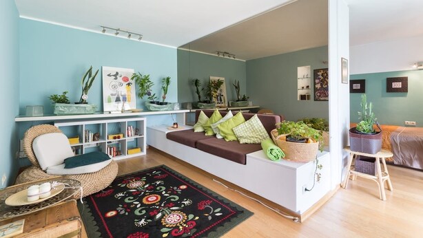 A modern living room with a sofa, a coffee table, and a bookshelf. There are several potted plants and a decorative rug. - Garden Studio 55 s.m. (Chalandri)