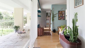 A spacious living area with a wooden floor, a white chair, a small table, and a potted plant. - Garden Studio 55 s.m. (Chalandri)