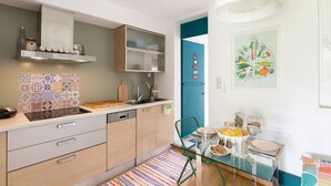 A modern kitchen with a tiled backsplash, wooden cabinets, a glass dining table, and a colorful rug. - Garden Studio 55 s.m. (Chalandri)