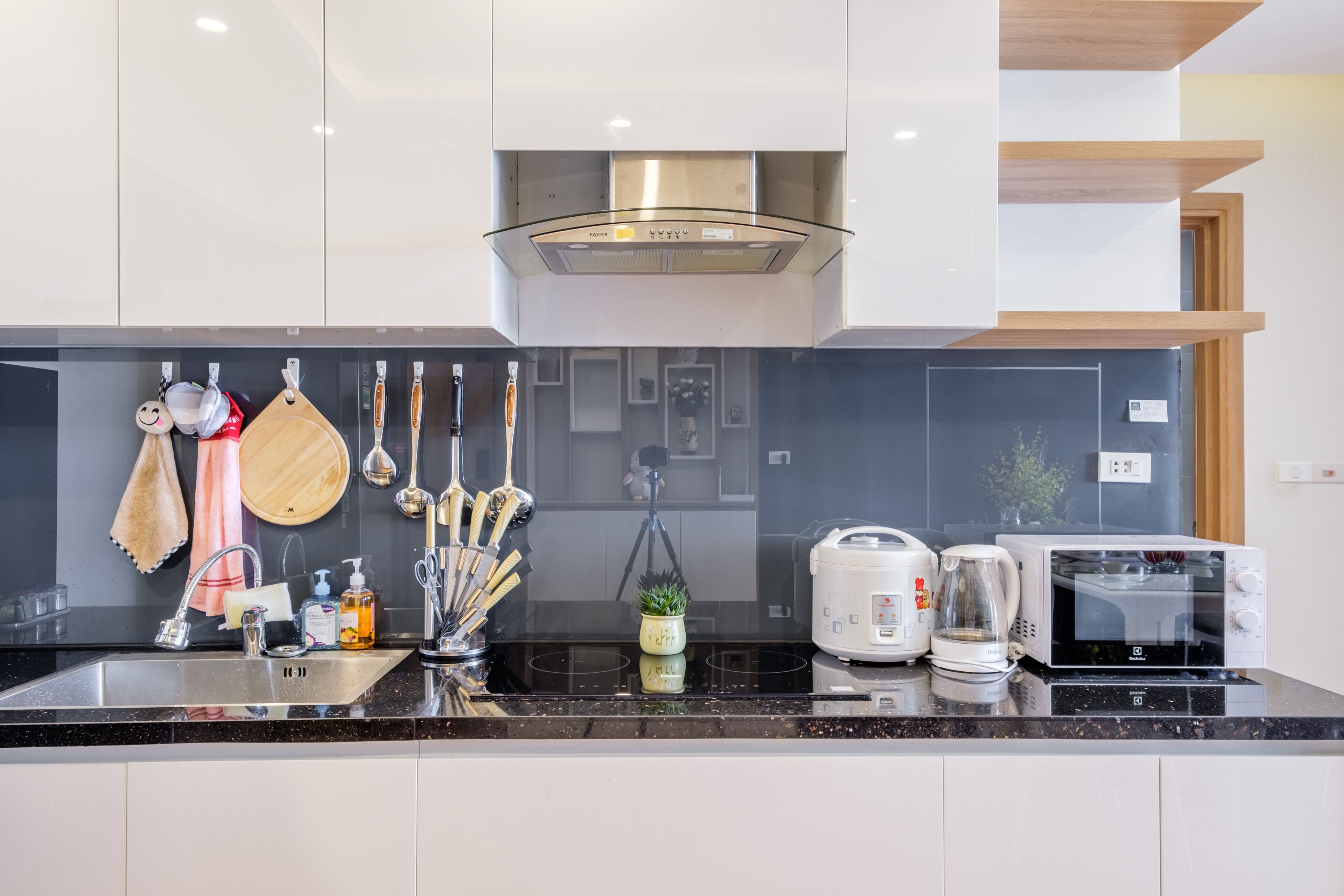 A modern kitchen with a black countertop, stainless steel sink, and white cabinets. There is a microwave, toaster, and coffee maker on the counter.