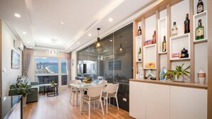 A modern kitchen with a dining area, a glass wall with a city view, and a wine shelf. - Apartment SeaView at Muong Thanh Residence (Da Nang)