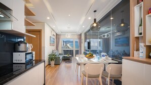 A modern kitchen with a dining area, featuring a black countertop, white cabinets, and a dining table with chairs. - Apartment SeaView at Muong Thanh Residence (Da Nang)