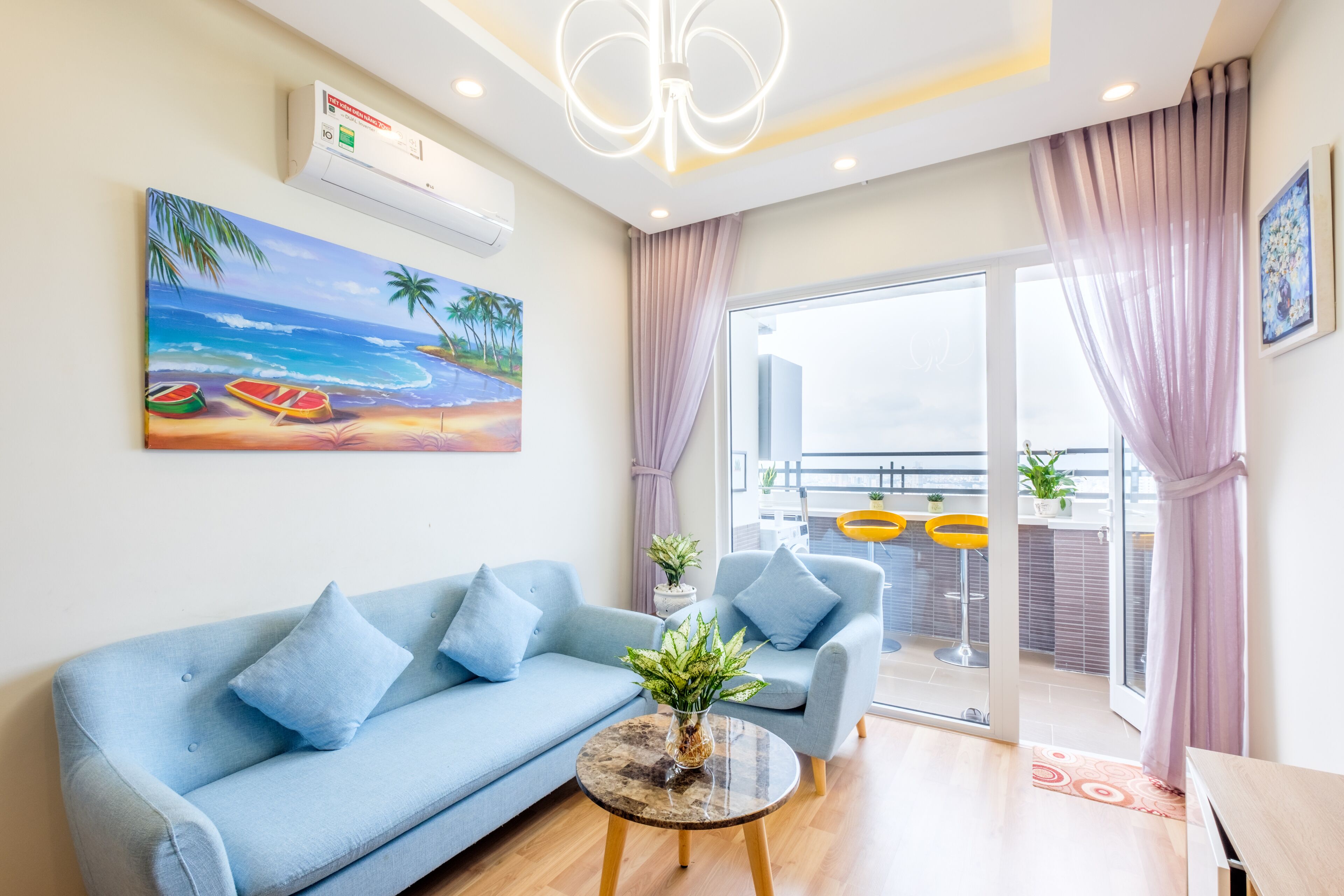Uma sala de estar moderna com um sofá azul, uma mesa de centro e um quadro com uma paisagem praiana.
