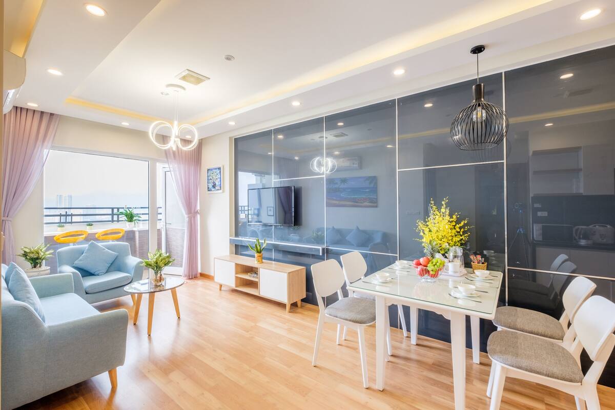 A modern living room with a dining area, large windows, and a TV.