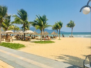 A beachside area with palm trees, beach chairs, and umbrellas. - Apartment SeaView at Muong Thanh Residence (Da Nang)