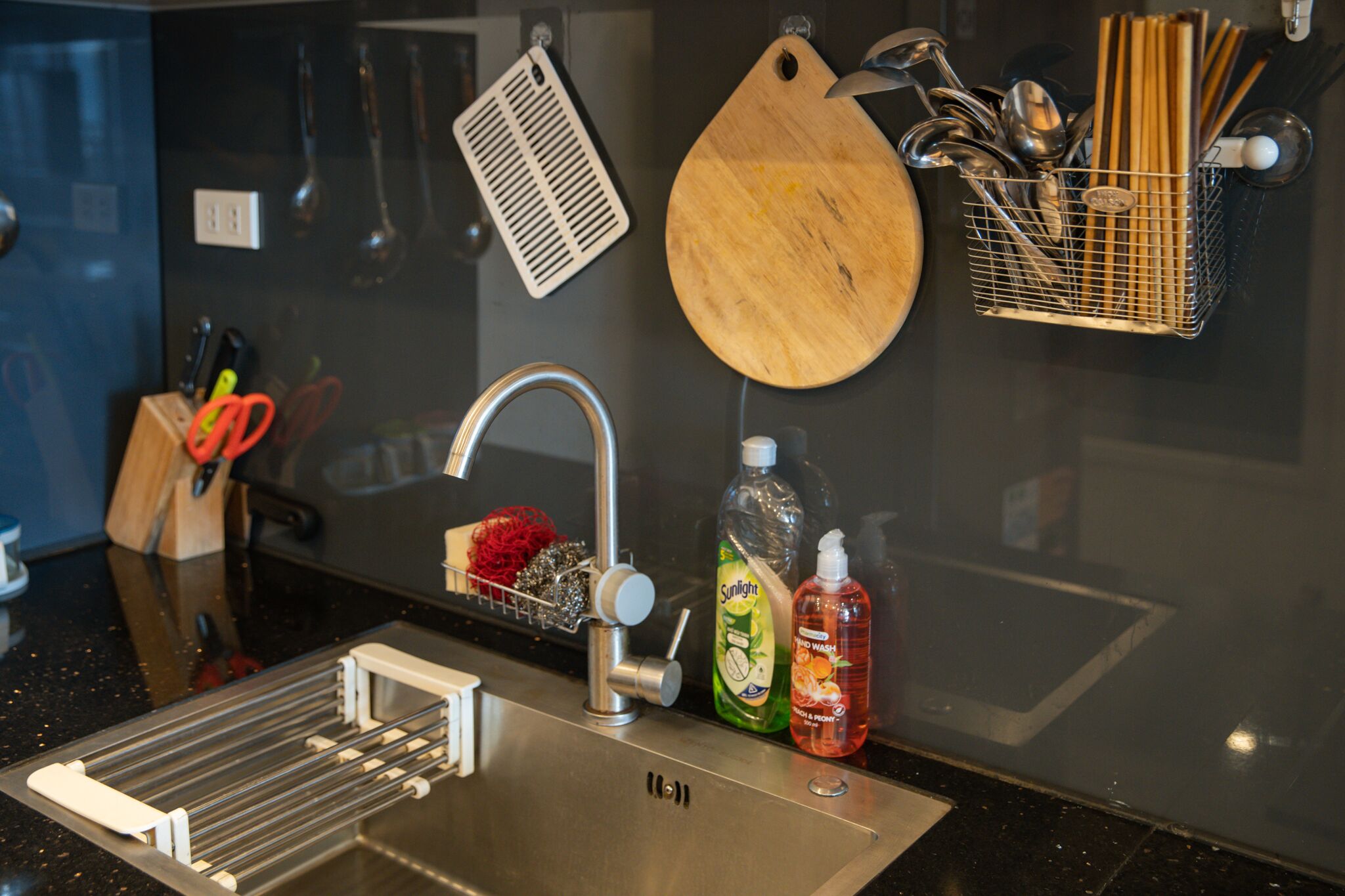 A kitchen with a stainless steel sink, a wooden cutting board, and a utensil holder.