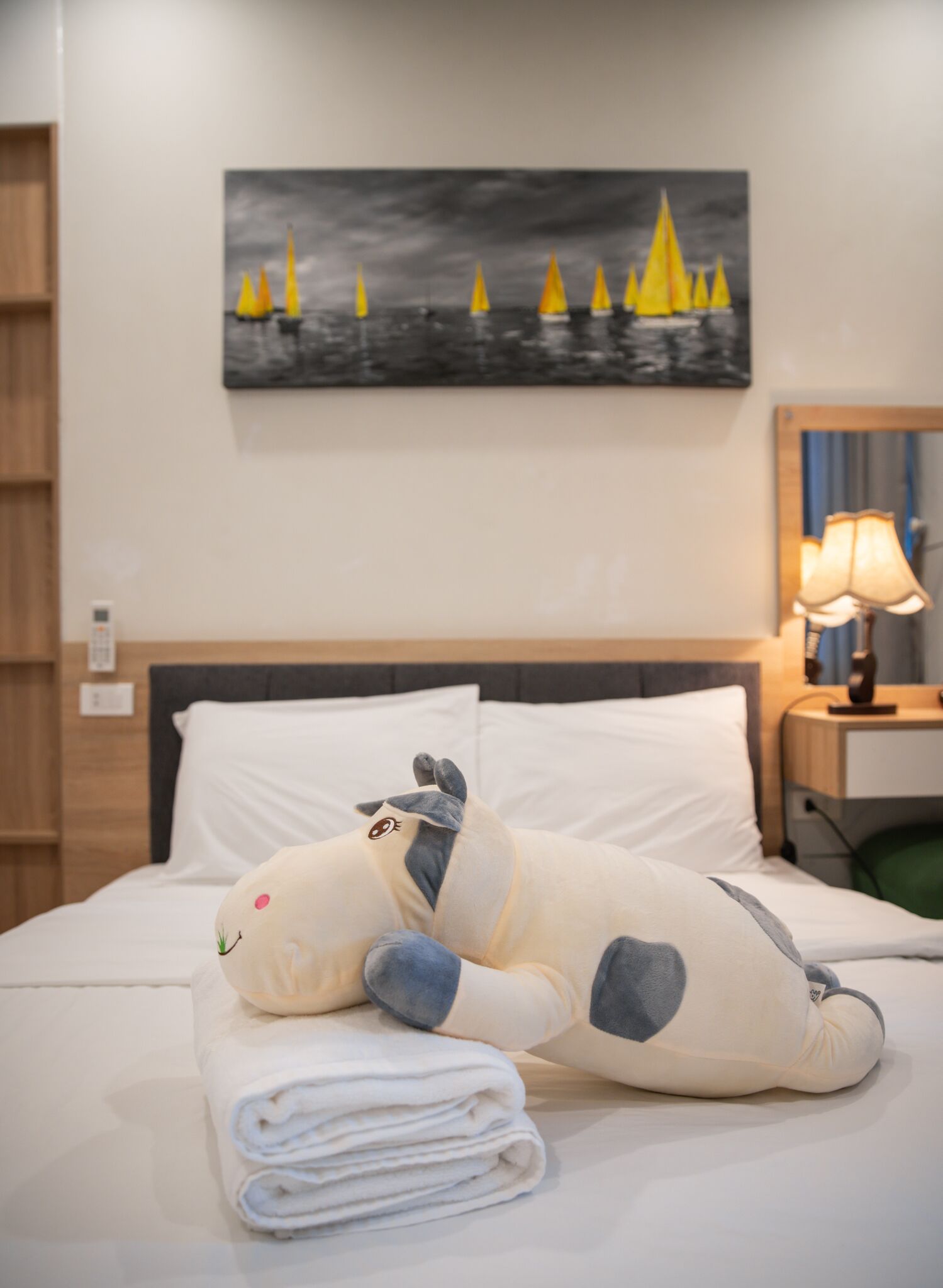 Un letto ben rifatto con un peluche, un quadro con dei velieri sulla parete e una lampada su un comodino.