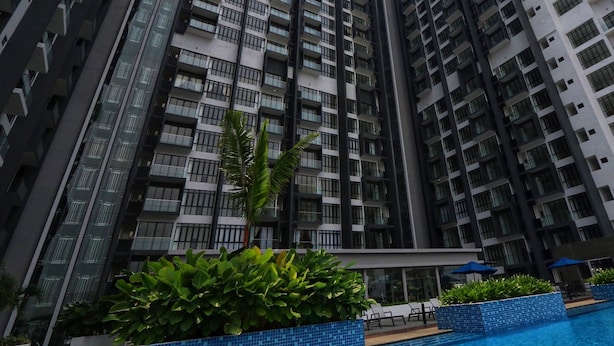 Un edificio residencial alto con múltiples balcones, un área de piscina con sillones de descanso y abundante vegetación.