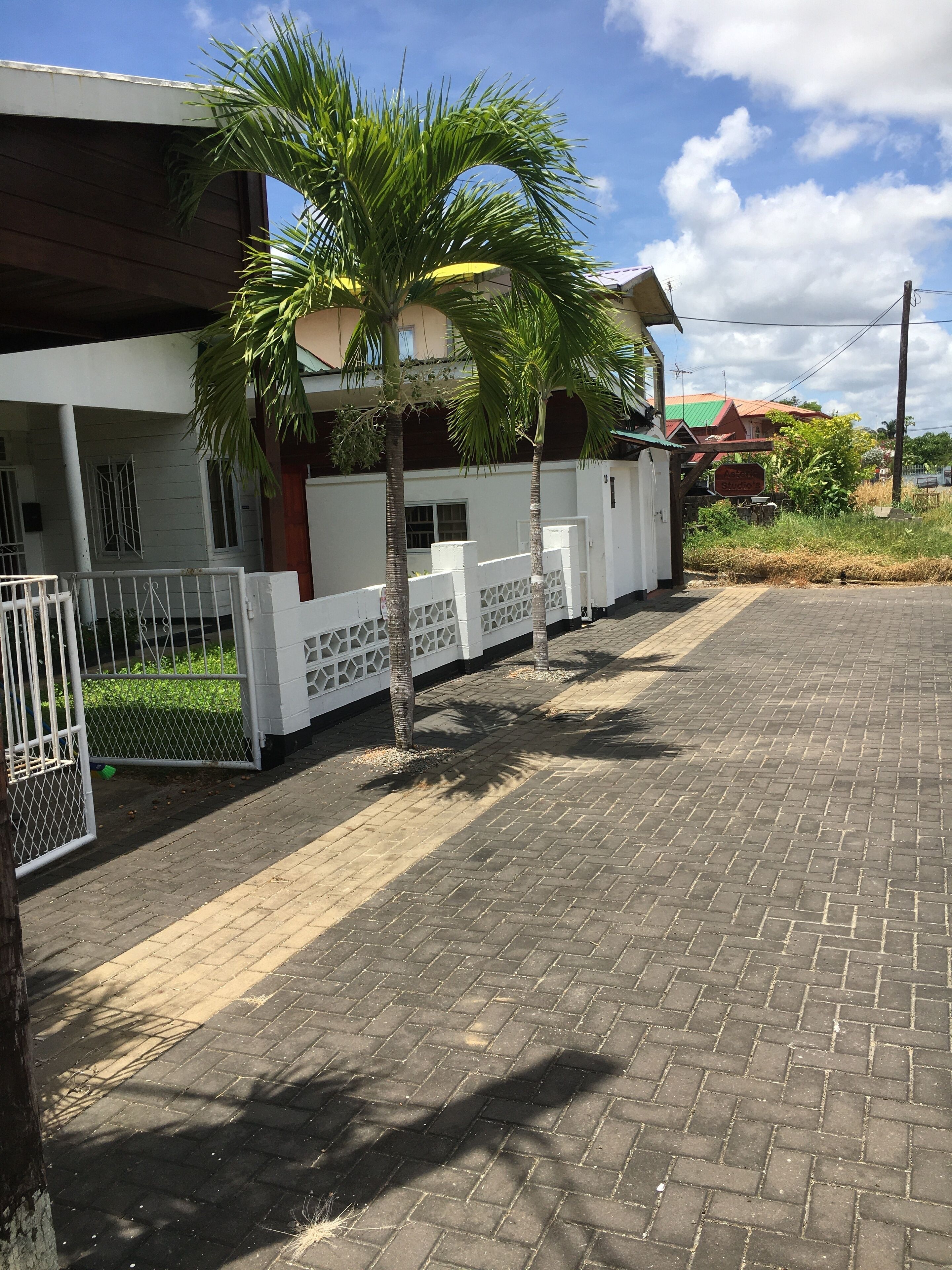 Un área pavimentada con cerca blanca, palmeras y un edificio de techo rojo.