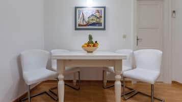 A dining area with a white table, two white chairs, a fruit bowl, and a painting on the wall.