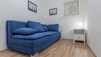 A room with a blue sofa, a white nightstand with a lamp, and two framed pictures on the wall.