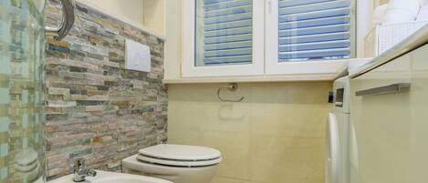 A bathroom with a sink, bidet, toilet, and a window with blinds.