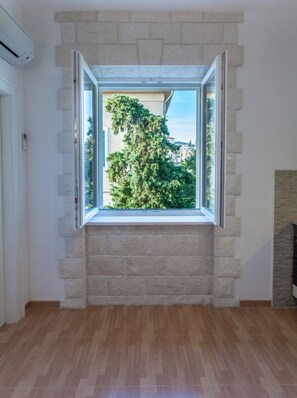 A room with a large window framed by stone blocks, a wooden floor, and a view of greenery and buildings outside. - Chic Apartment in Center (Split)