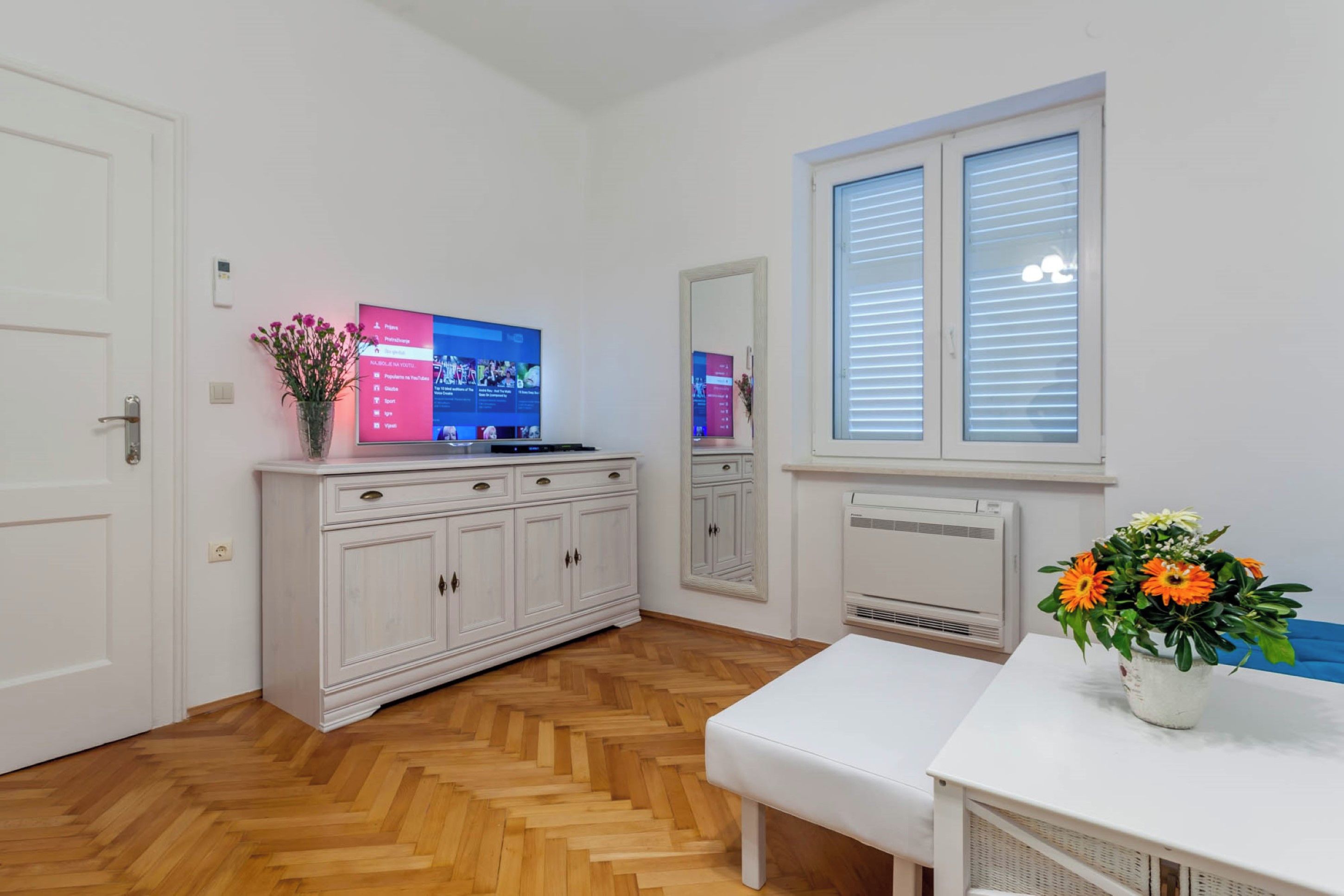 A modern kitchen with a white cabinet, a built-in TV, and a window with blinds.