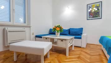 A room with a white bench, a blue sofa, a small table with a vase of flowers, and a wall-mounted light fixture.