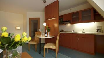 A compact kitchen with wooden cabinets, a dining area with two chairs, a small table, and a vase with yellow flowers.