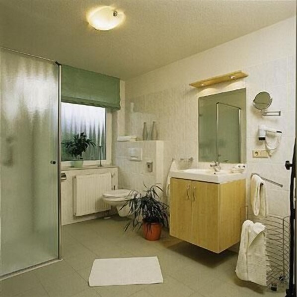 A bathroom with a toilet, sink, mirror, towel rack, and a potted plant. - Grothenn's Hotel (Bremen)