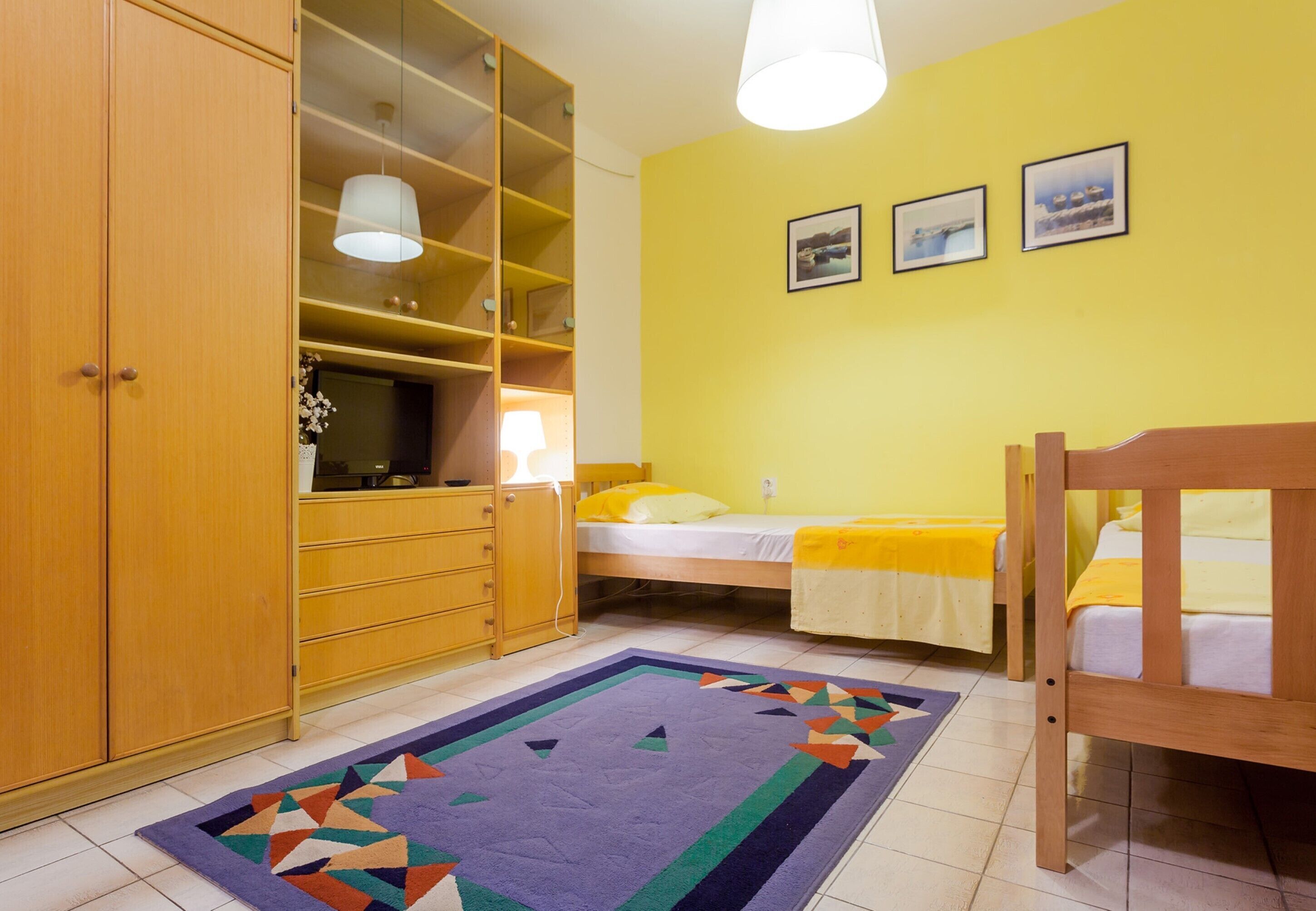 A bedroom with a bed, a wooden wardrobe, a desk, and a chair.