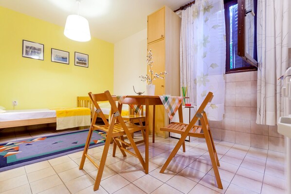 A room with a bed, a dining table with chairs, a small table with a plant, a window with curtains, and a wall with framed pictures. - Guest House Marija in perfect location (Split)